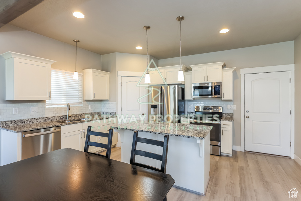 Kitchen featuring stainless steel appliances, a sink, decorative backsplash, light wood-style floors, and white cabinets