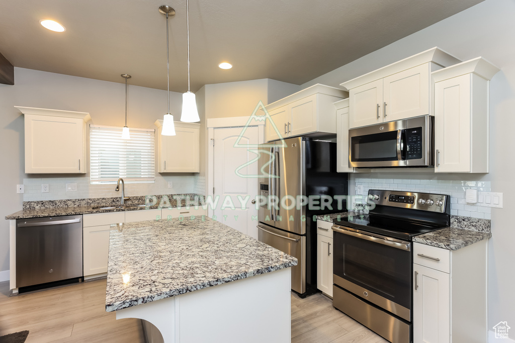 Kitchen with stainless steel appliances, a sink, tasteful backsplash, a center island, and white cabinets