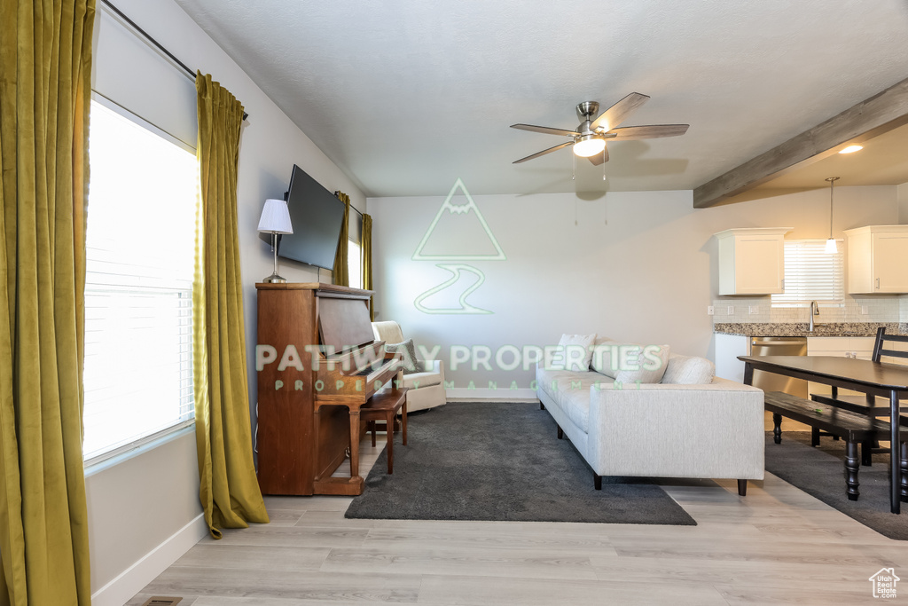 Living room with a ceiling fan, plenty of natural light, baseboards, beamed ceiling, and light wood-style floors