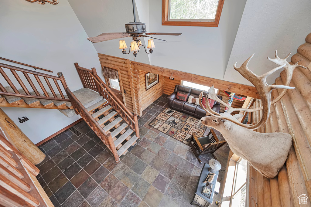Living room with stone tile flooring, ceiling fan, stairway, and a towering ceiling