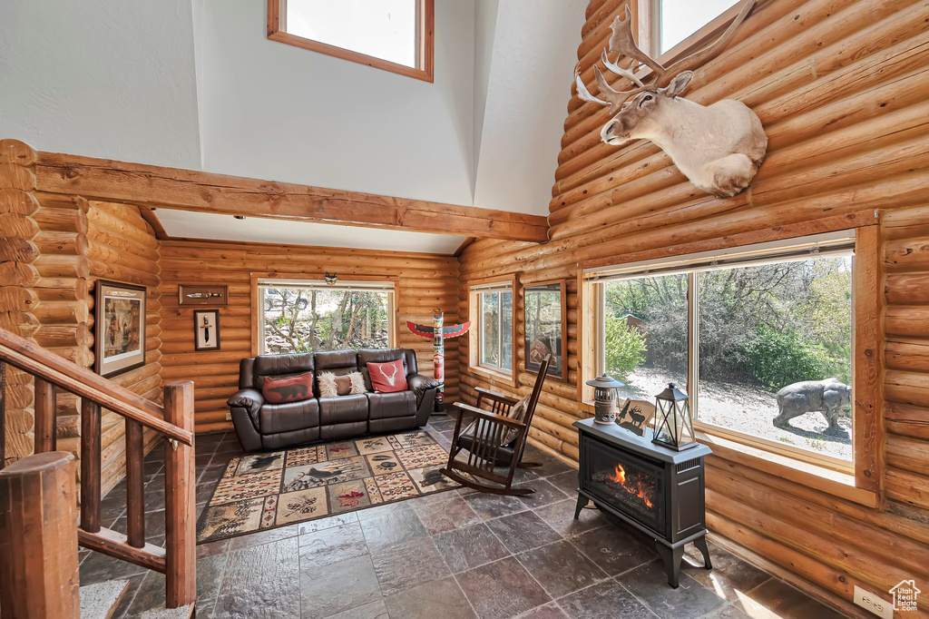 Living room featuring a towering ceiling, a wood stove, rustic walls, stairway, and dark stone finish flooring