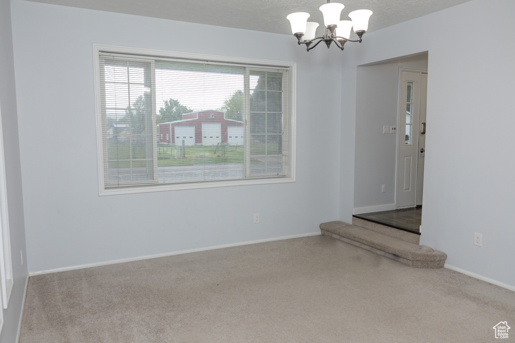 Empty room featuring carpet flooring, a chandelier, and baseboards