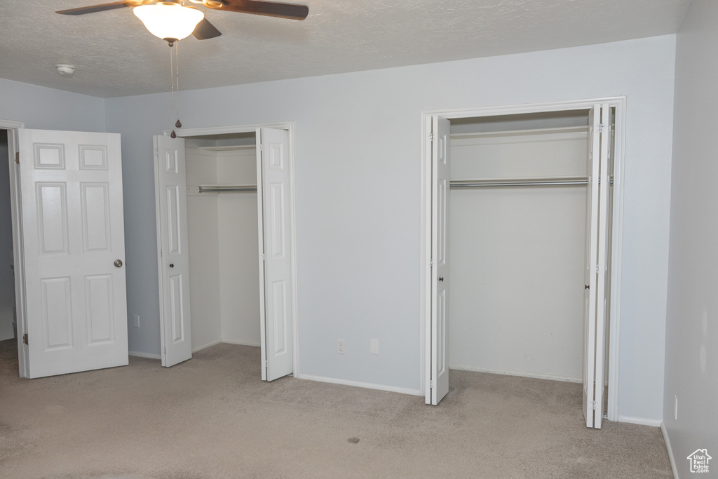 Unfurnished bedroom featuring two closets, carpet flooring, baseboards, and a textured ceiling