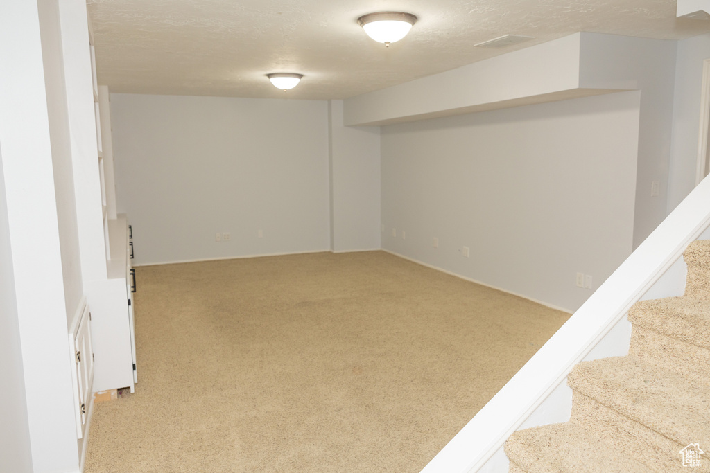 Finished below grade area with light colored carpet, stairs, and a textured ceiling
