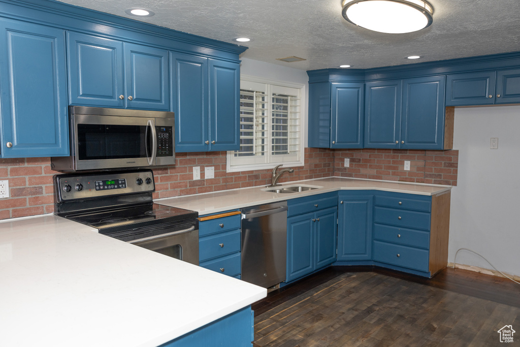 Kitchen with stainless steel appliances, a sink, blue cabinetry, decorative backsplash, and light countertops