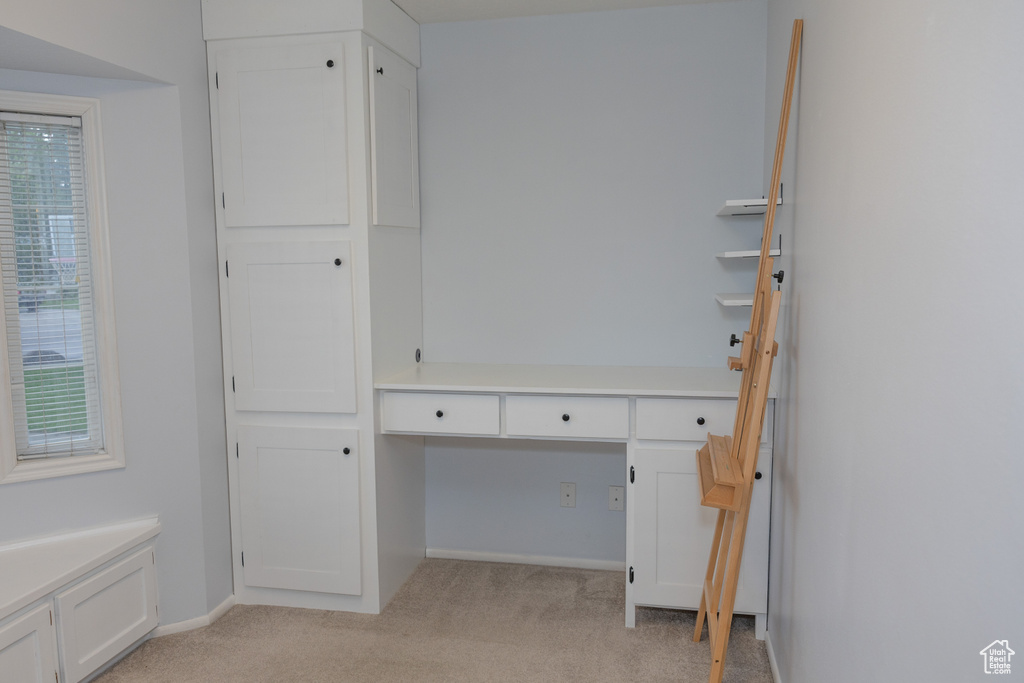 Unfurnished office featuring light carpet, built in desk, and baseboards