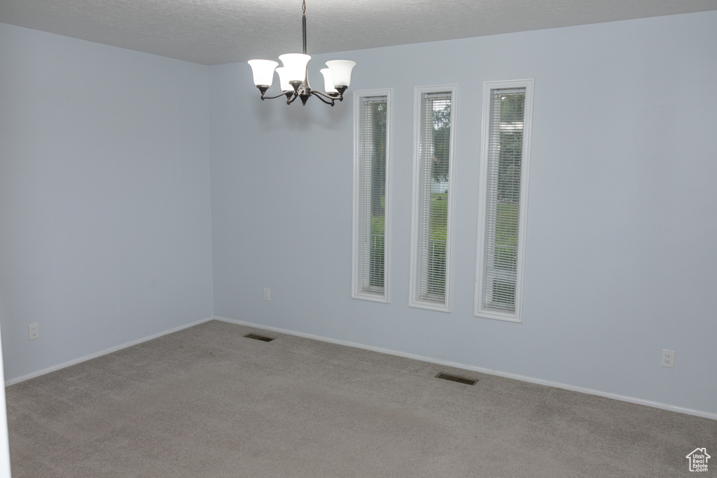Unfurnished room featuring a chandelier, carpet floors, baseboards, and a textured ceiling