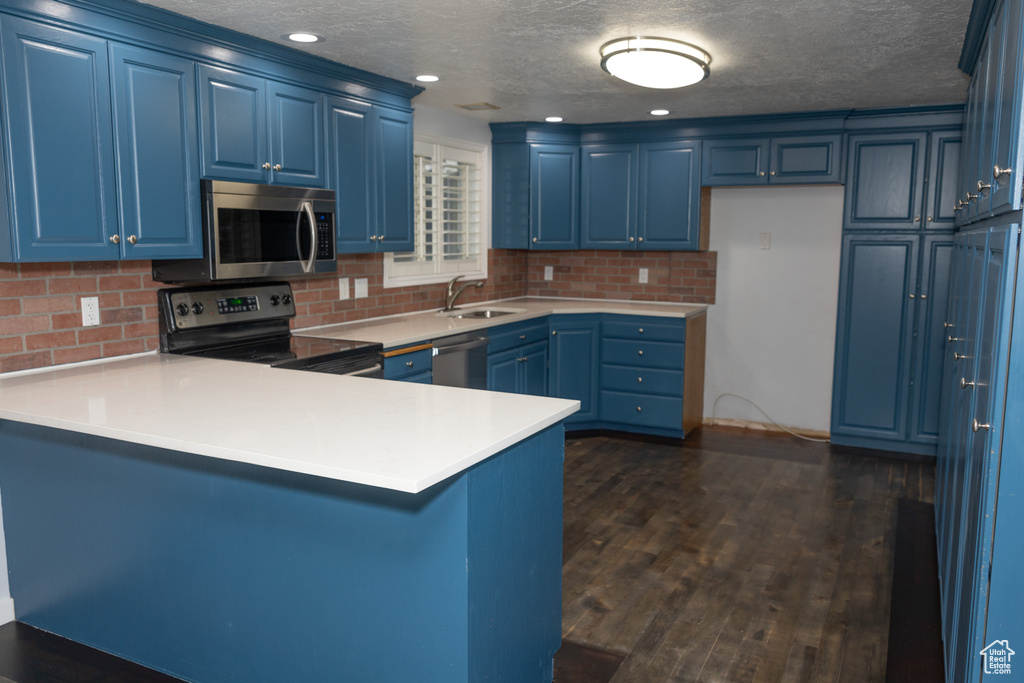 Kitchen featuring appliances with stainless steel finishes, blue cabinets, a peninsula, a sink, and a textured ceiling