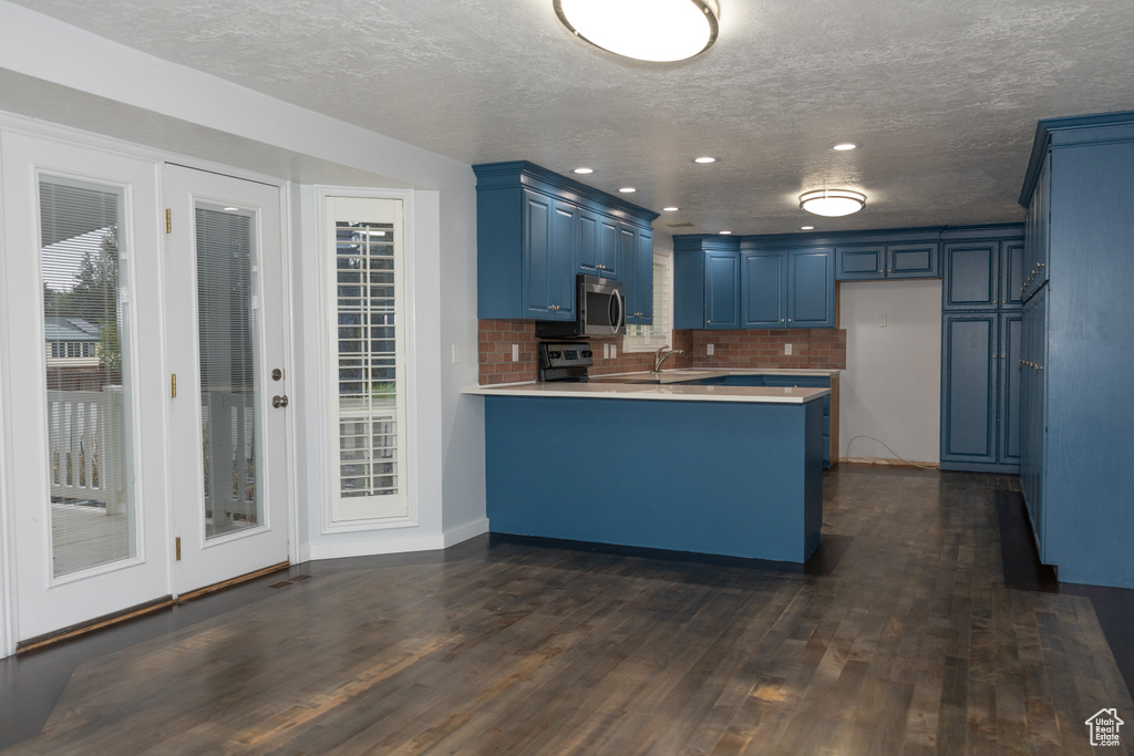 Kitchen featuring blue cabinets, a peninsula, appliances with stainless steel finishes, dark wood-style flooring, and a sink