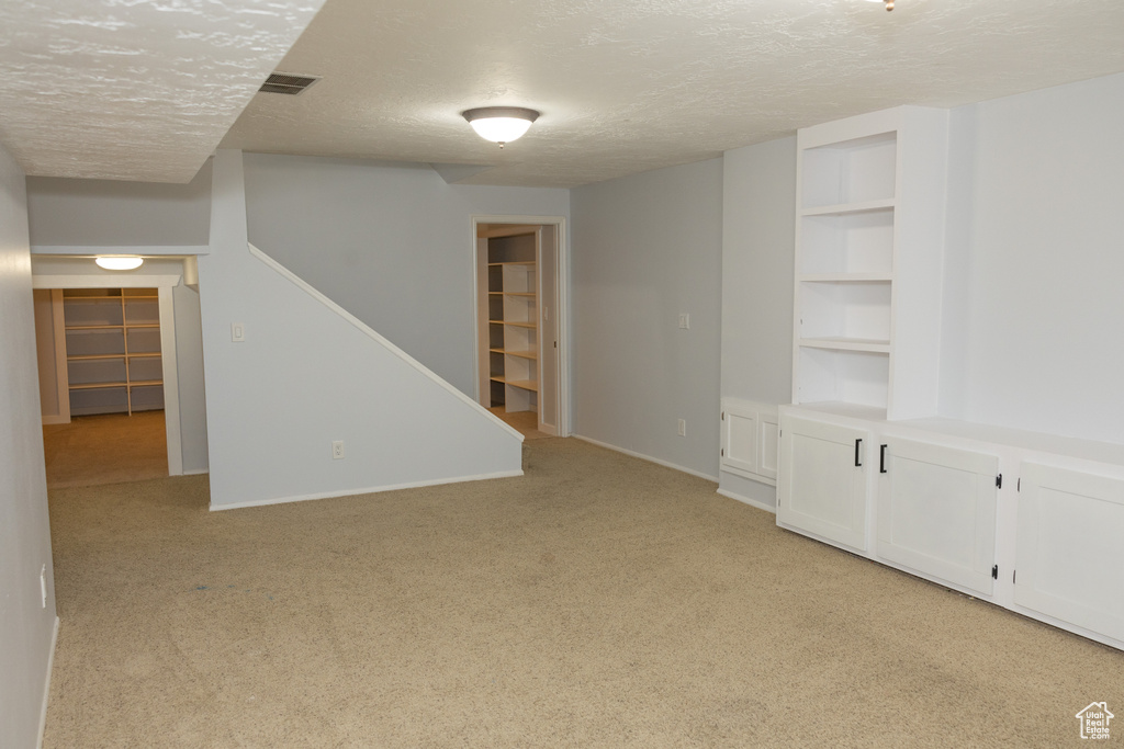 Spare room with light carpet, a textured ceiling, stairway, built in shelves, and baseboards