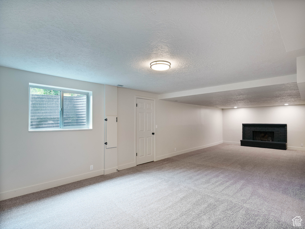 Unfurnished living room with a textured ceiling, a fireplace, baseboards, and carpet flooring