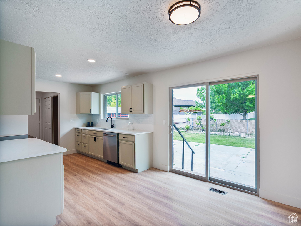 Kitchen featuring a sink, light wood-style flooring, stainless steel dishwasher, light countertops, and a textured ceiling