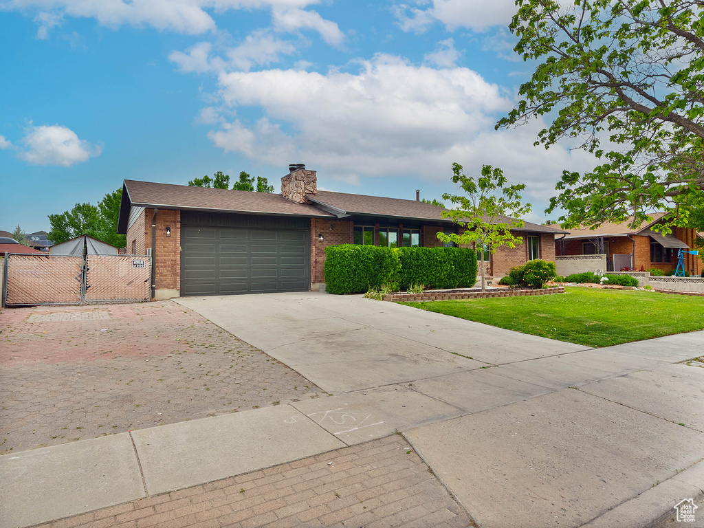 Ranch-style home featuring driveway, a chimney, brick siding, and an attached garage