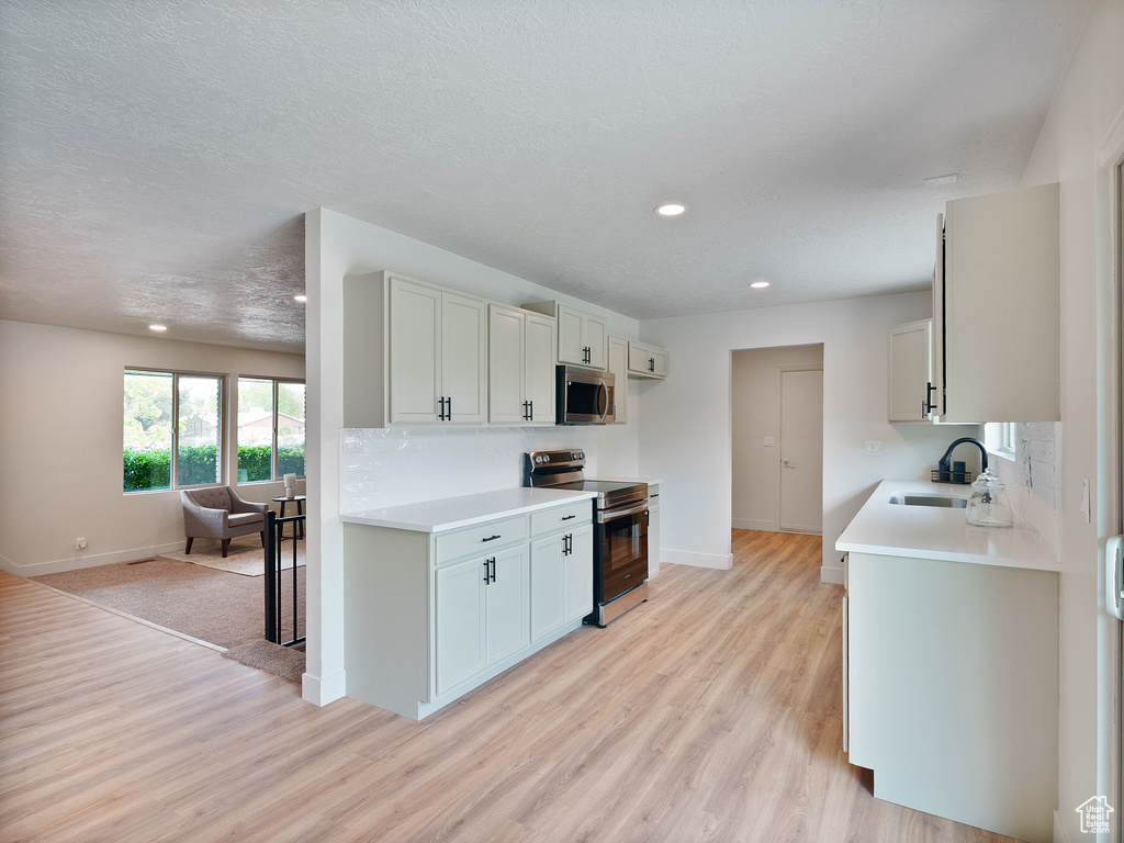 Kitchen with appliances with stainless steel finishes, baseboards, a sink, light wood-style floors, and recessed lighting