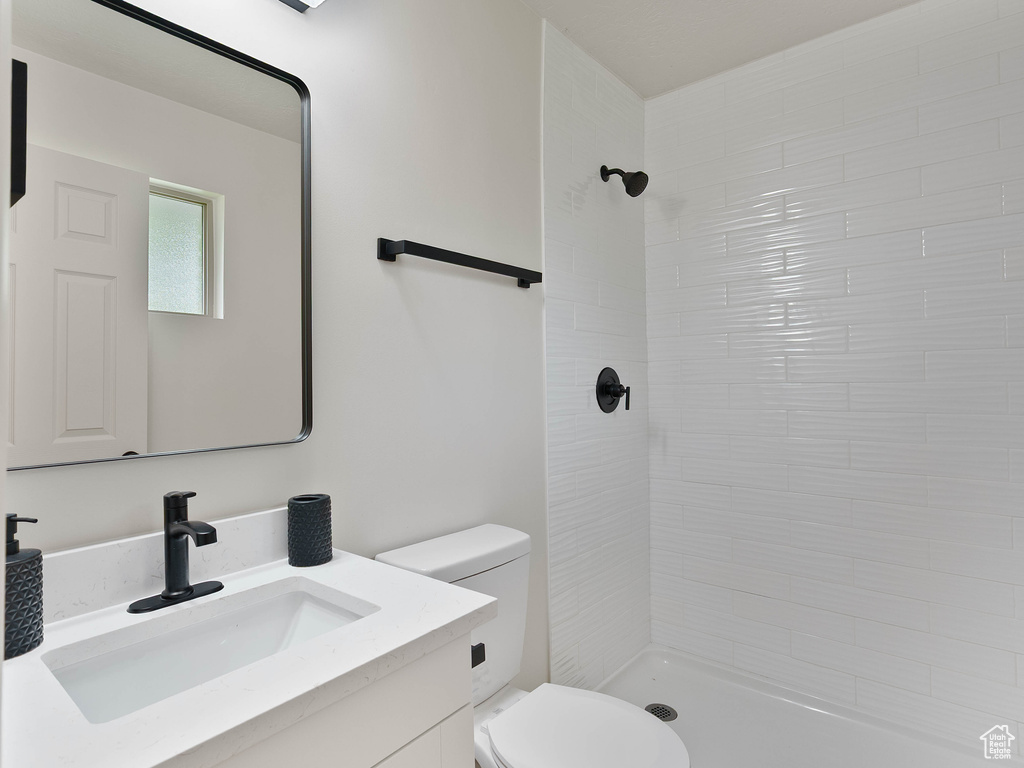 Bathroom with toilet, a tile shower, and vanity