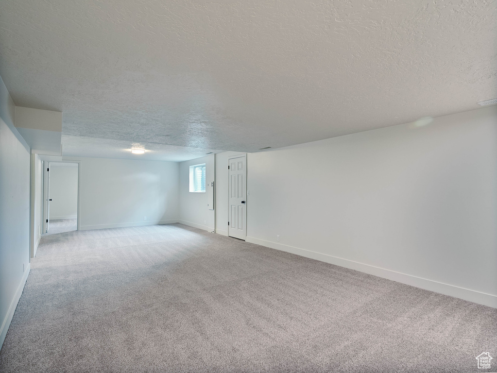 Unfurnished room with a textured ceiling, light carpet, and baseboards