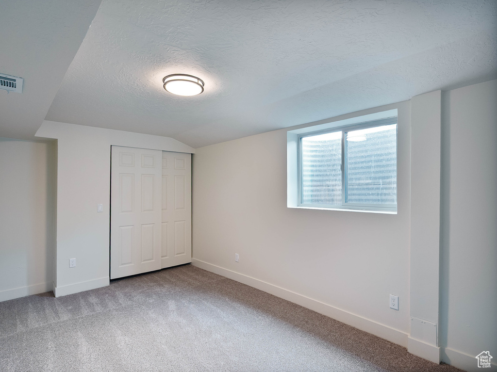 Unfurnished bedroom with a textured ceiling, carpet, a closet, lofted ceiling, and baseboards