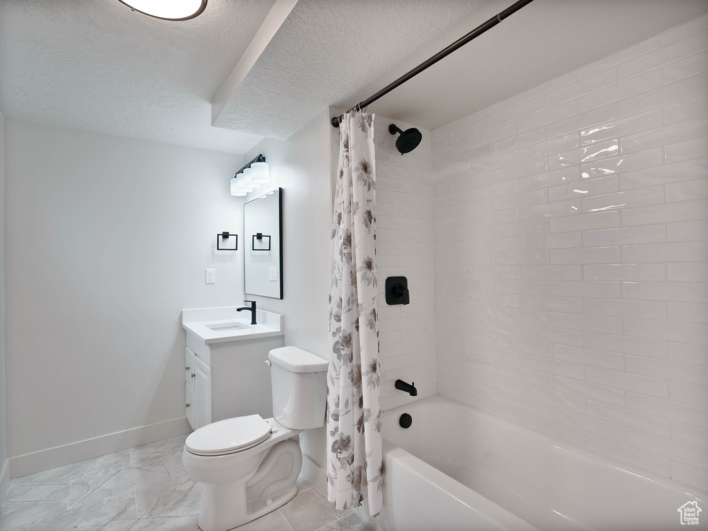 Full bath with baseboards, a textured ceiling, toilet, shower / bath combo with shower curtain, and vanity