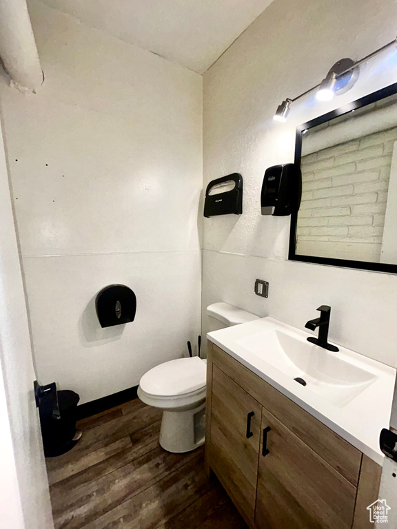 Half bathroom featuring wood finished floors, vanity, and toilet