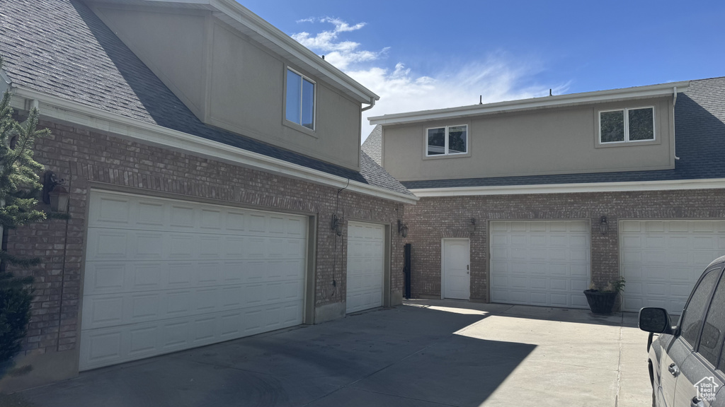 View of front of house featuring brick siding, a garage, a shingled roof, and stucco siding