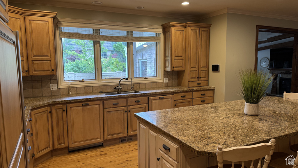 Kitchen with a sink, light wood-style flooring, backsplash, a breakfast bar, and crown molding
