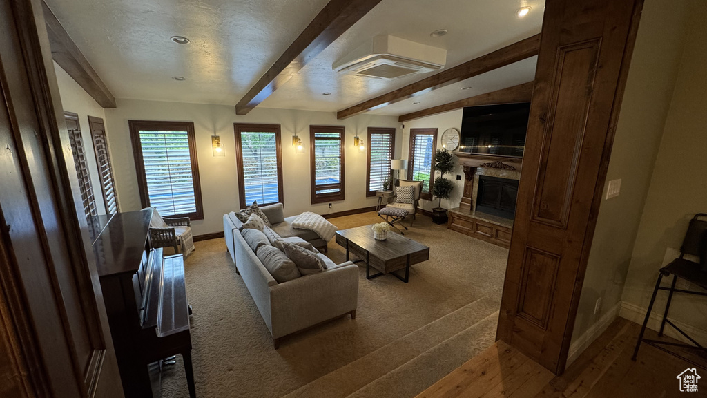 Living area featuring baseboards, a glass covered fireplace, beamed ceiling, and carpet flooring