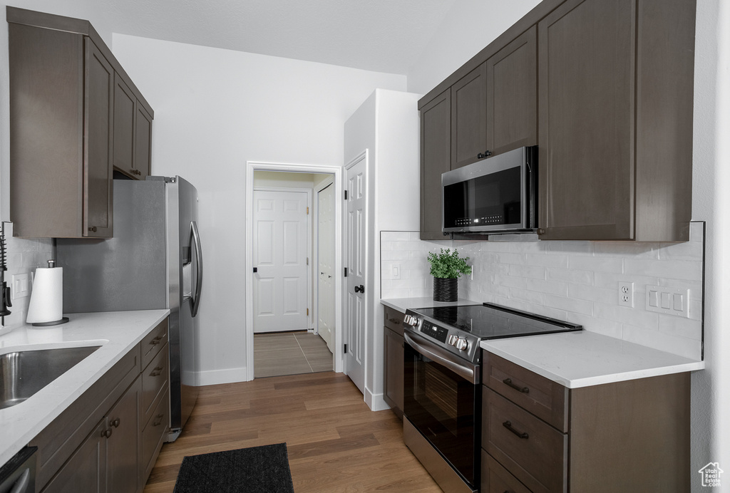 Kitchen featuring stainless steel appliances, decorative backsplash, light countertops, light wood finished floors, and baseboards