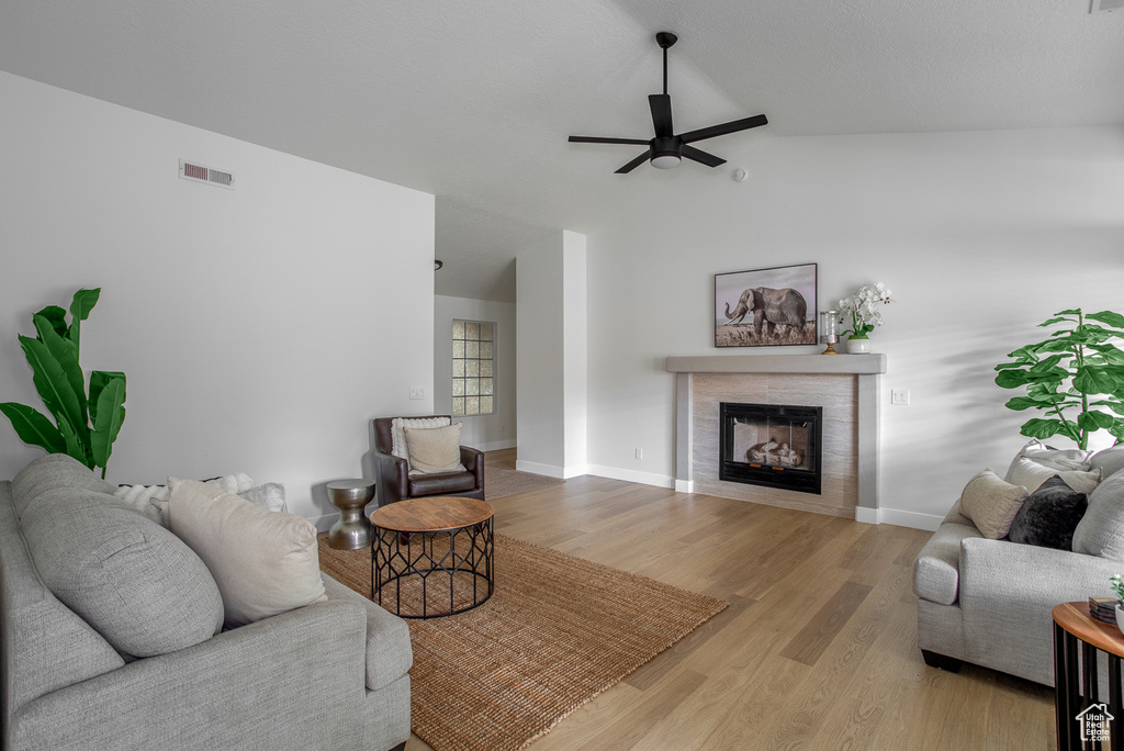 Living room with ceiling fan, a fireplace, lofted ceiling, light wood finished floors, and baseboards