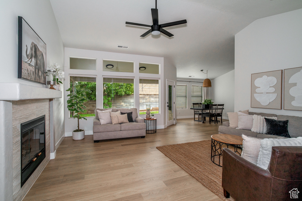 Living room with lofted ceiling, a fireplace, ceiling fan, light wood finished floors, and baseboards