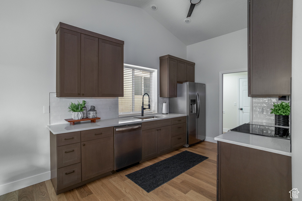 Kitchen with appliances with stainless steel finishes, a sink, backsplash, light countertops, and high vaulted ceiling