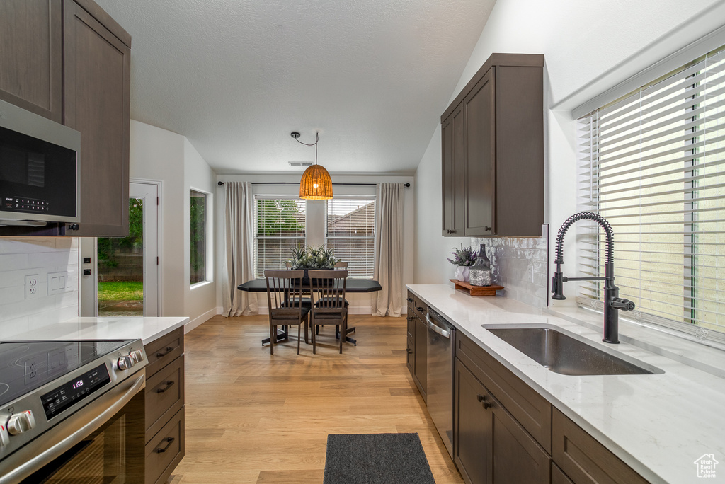 Kitchen featuring appliances with stainless steel finishes, a sink, backsplash, and dark brown cabinetry