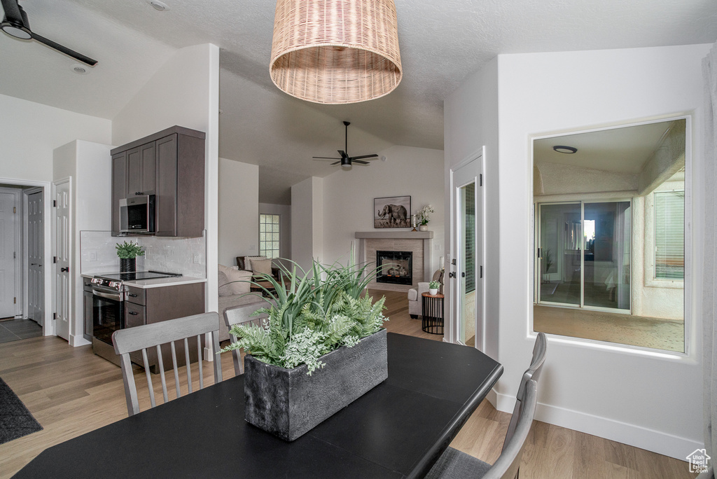 Dining space with lofted ceiling, a ceiling fan, light wood-style floors, baseboards, and a fireplace