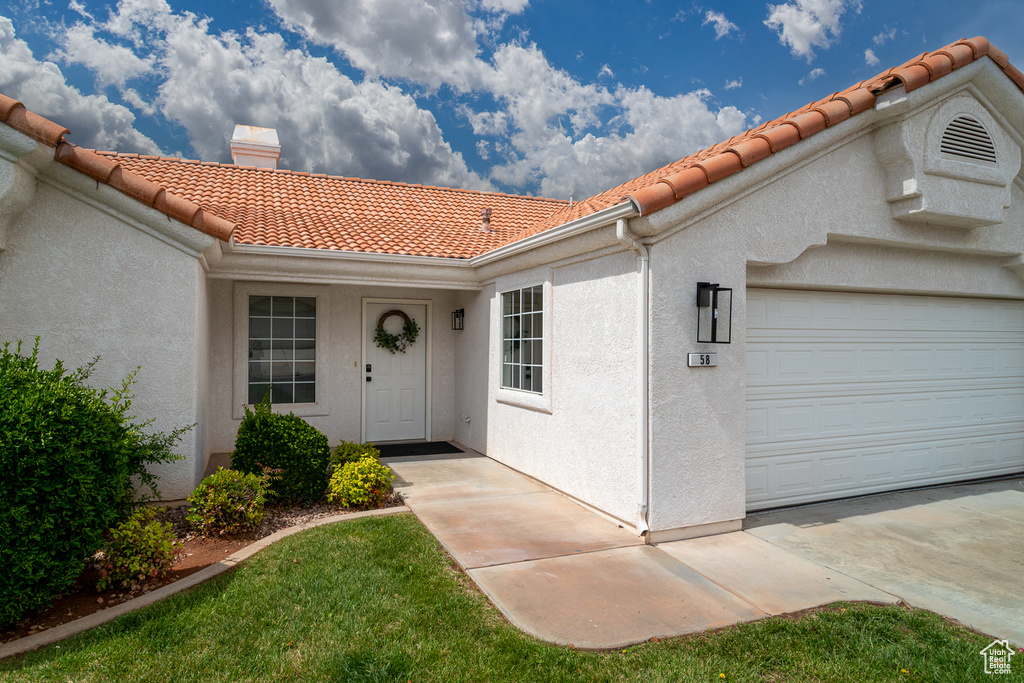 Doorway to property featuring a tiled roof, a chimney, stucco siding, and a garage