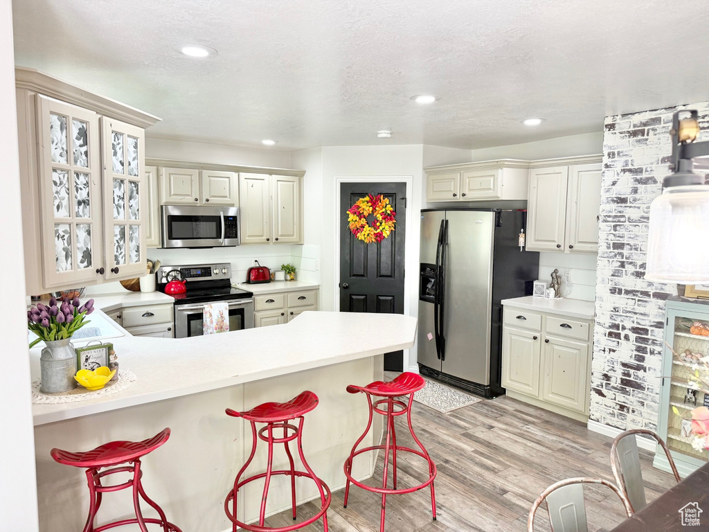 Kitchen featuring stainless steel appliances, a kitchen bar, light wood finished floors, light countertops, and a peninsula