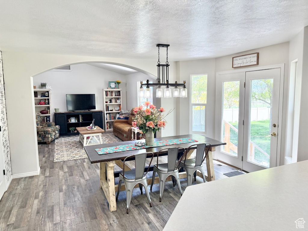 Dining area with wood finished floors, plenty of natural light, a textured ceiling, arched walkways, and baseboards