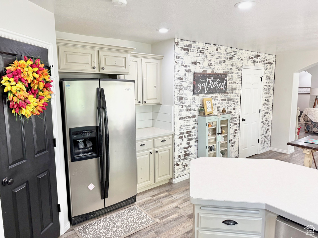 Kitchen featuring stainless steel fridge with ice dispenser, light countertops, arched walkways, light wood-type flooring, and cream cabinetry