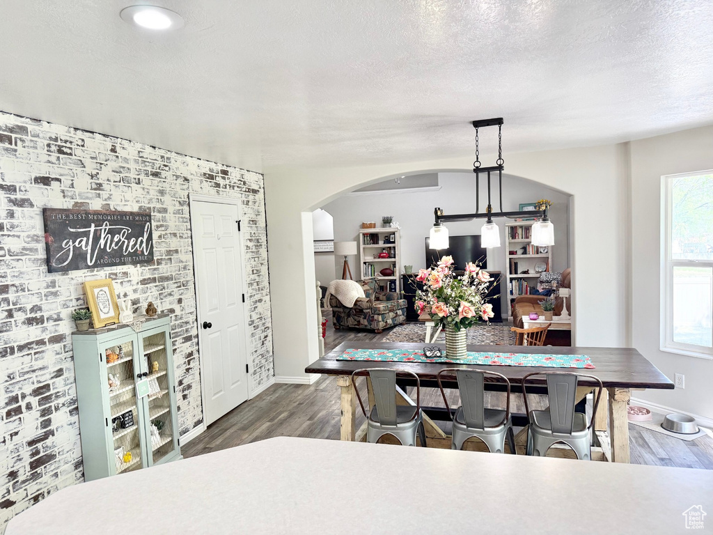 Dining room featuring wood finished floors, arched walkways, baseboards, brick wall, and a textured ceiling