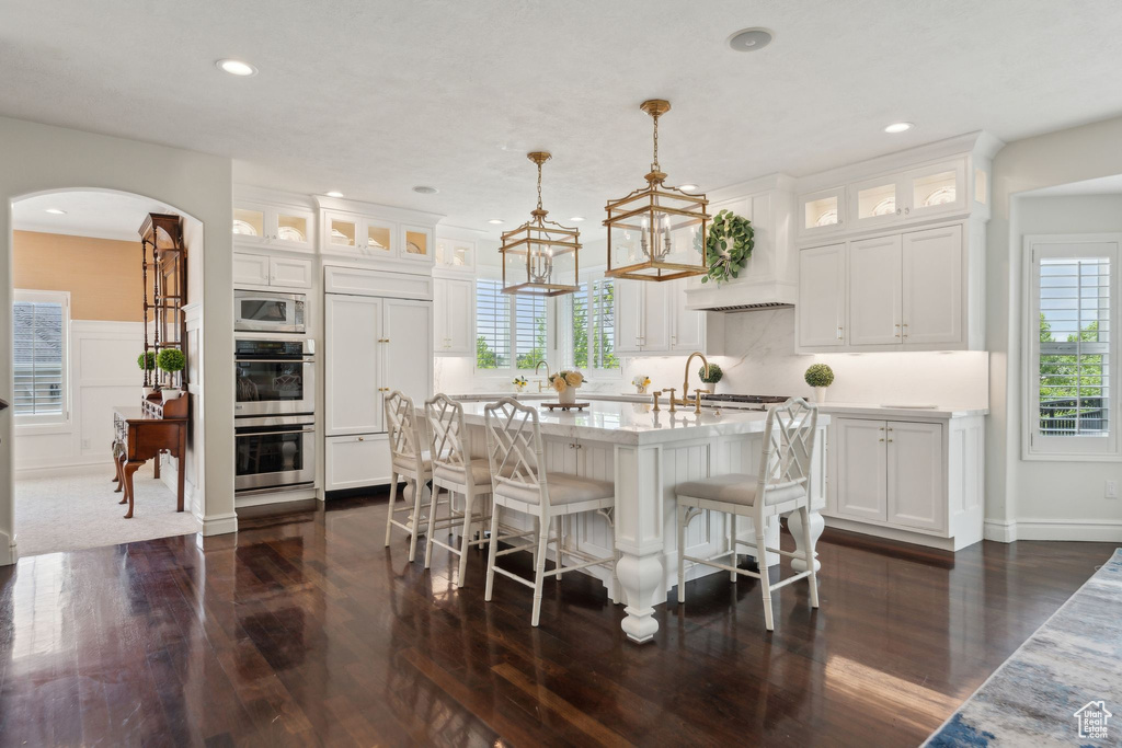 Kitchen with appliances with stainless steel finishes, dark wood-type flooring, arched walkways, white cabinetry, and recessed lighting