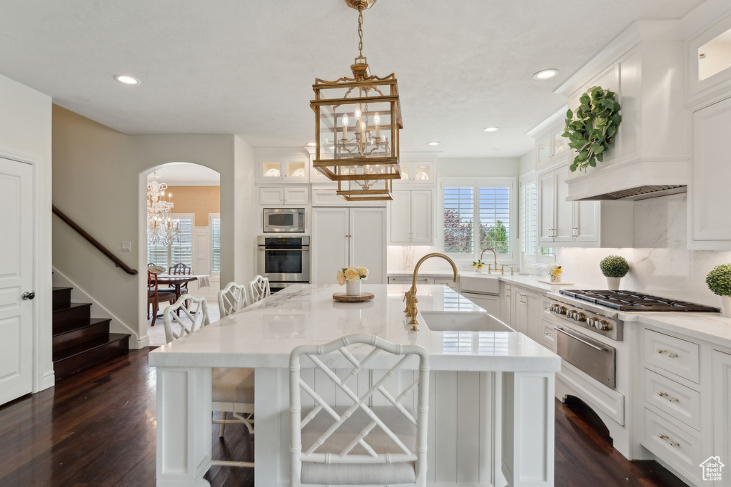 Kitchen with stainless steel appliances, a chandelier, arched walkways, a warming drawer, and white cabinets