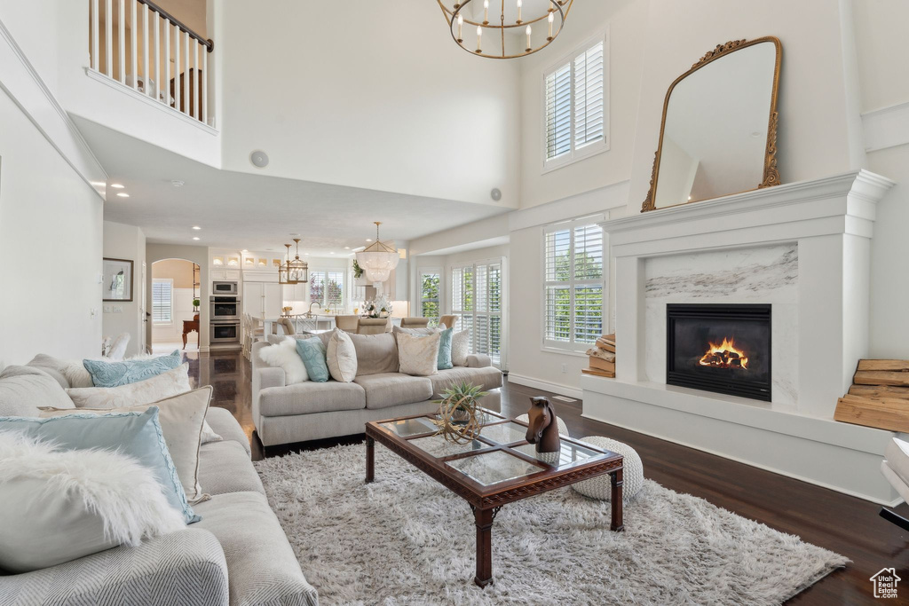 Living area featuring a chandelier, dark wood finished floors, a high ceiling, a premium fireplace, and plenty of natural light