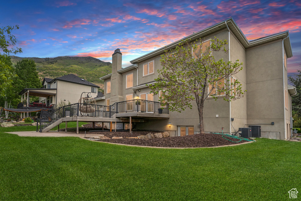 Back of house with stairs, stucco siding, a lawn, and a deck with mountain view