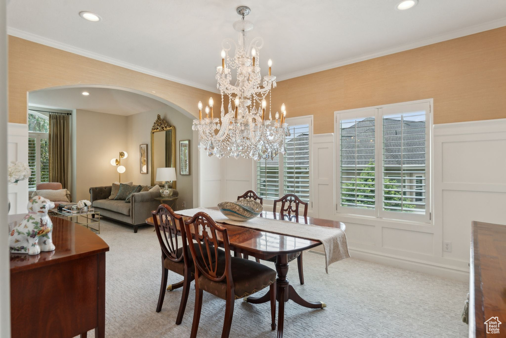 Dining room with a decorative wall, arched walkways, light carpet, a chandelier, and crown molding