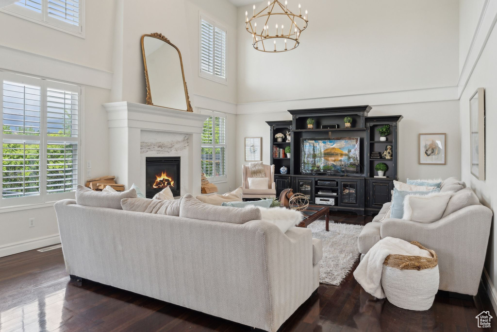 Living room featuring a towering ceiling, a chandelier, a high end fireplace, dark wood-style flooring, and baseboards