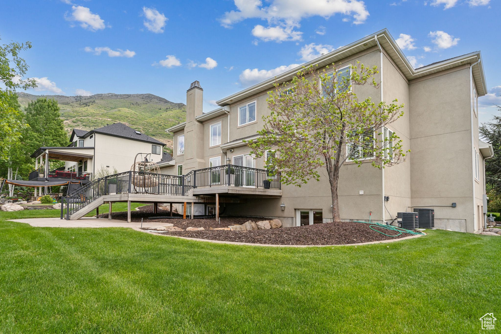 Rear view of house with a deck with mountain view, a yard, stucco siding, and stairway