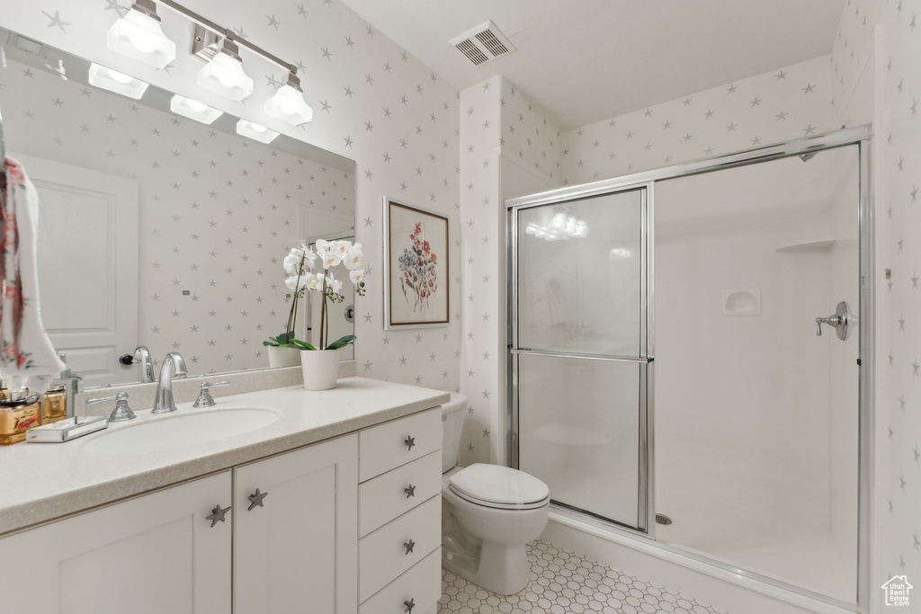 Bathroom with wallpapered walls, a shower stall, toilet, vanity, and tile patterned floors