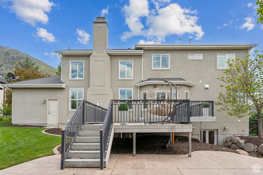 Back of property featuring stucco siding, a deck, a chimney, a lawn, and stairs