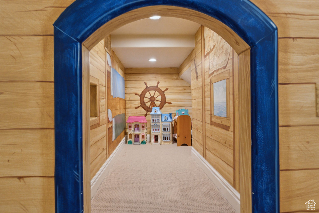 Recreation room with carpet, arched walkways, wood walls, and baseboards