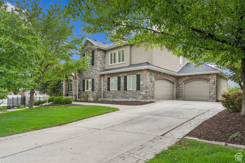 View of front of house featuring stone siding, driveway, stucco siding, and a garage