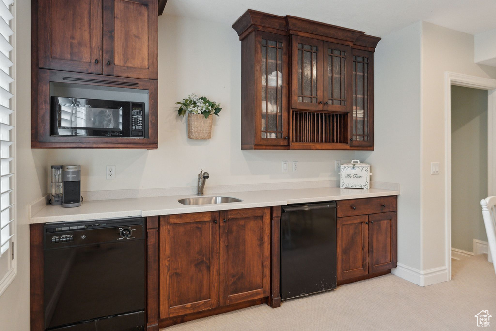 Kitchen featuring black appliances, a sink, light countertops, glass insert cabinets, and light colored carpet