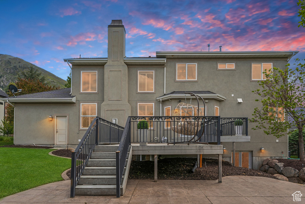 Rear view of property featuring stucco siding, a wooden deck, a chimney, a yard, and stairway